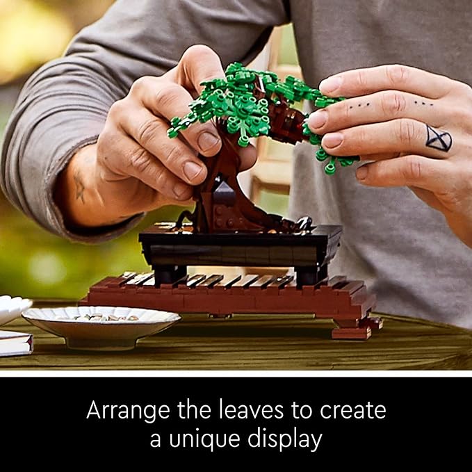 A person assembles a LEGO Bonsai Tree model, adjusting green leaves on a brown base for a customizable display.