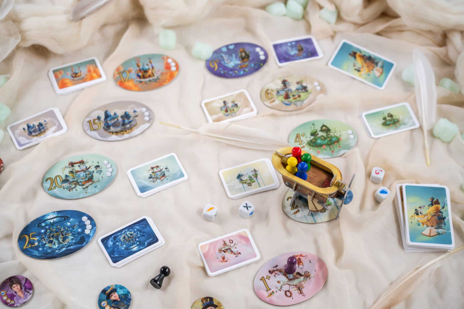 Colorful game components of Celestia spread out on a soft surface, featuring cards, tokens, and a miniature airship.