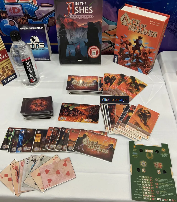 Ace of Spades board game preorder display featuring cards, rulebook, and gaming accessories on a table.