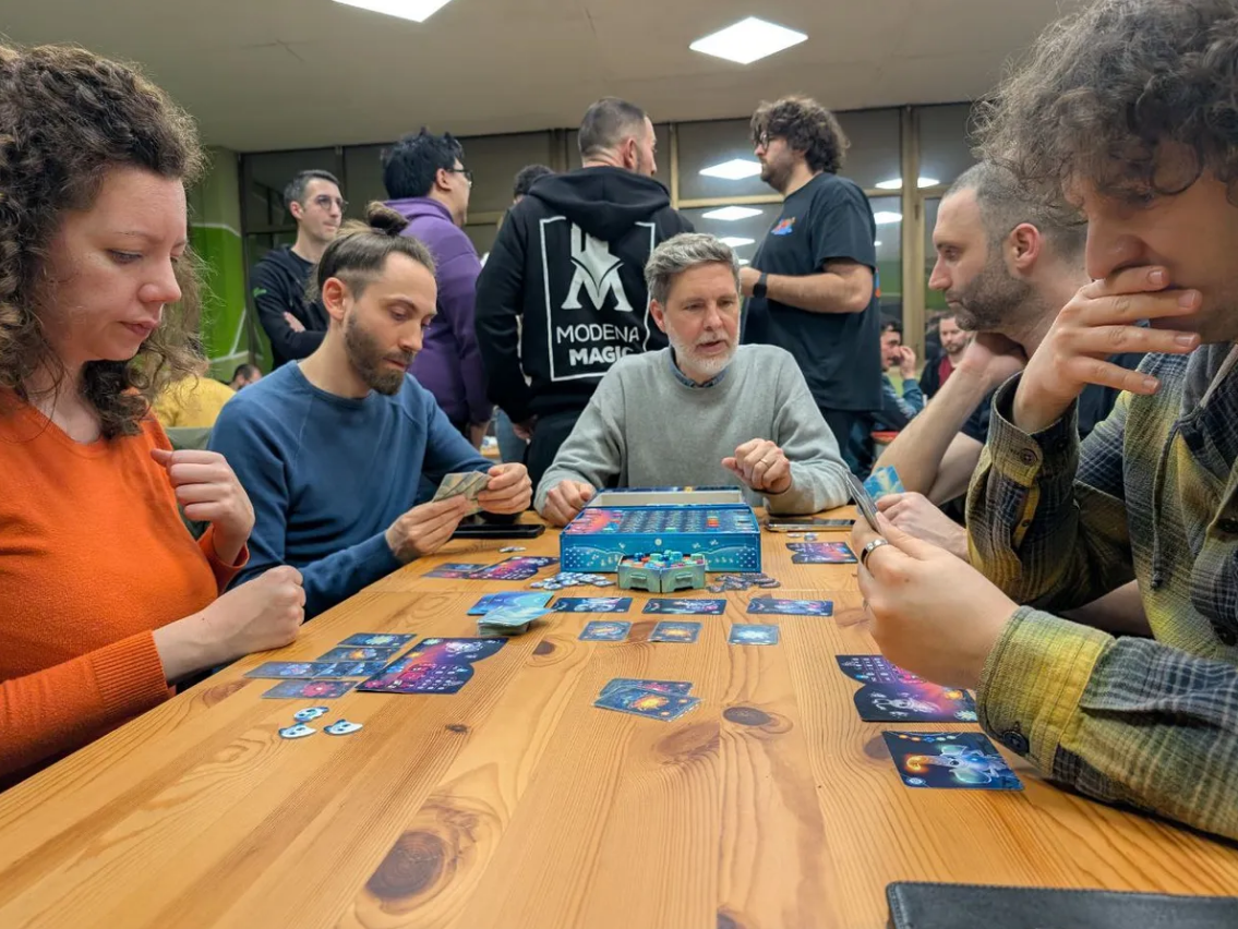 Group of players engaged in a tabletop game session of Gloomies, with cards and game pieces spread on a wooden table.