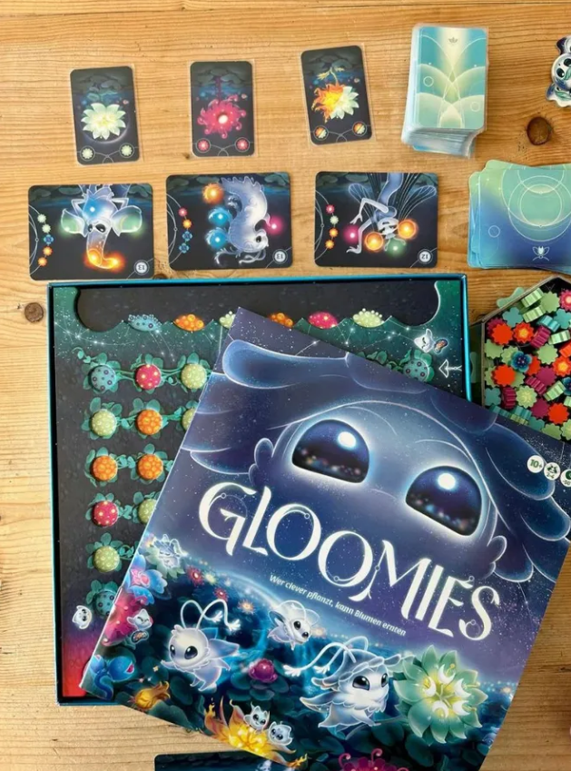 Gloomies board game with colorful cards and game pieces displayed on a wooden table, featuring whimsical artwork.