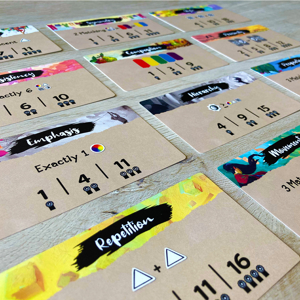 Colorful game cards from the Canvas board game, featuring various artistic prompts and scoring details laid out on a wooden surface.
