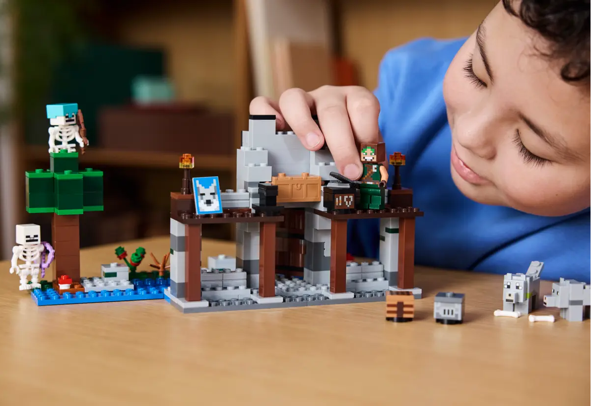 Child playing with LEGO Minecraft The Wolf Stronghold Fortress Playset 21261, featuring a fortress, skeletons, and accessories.