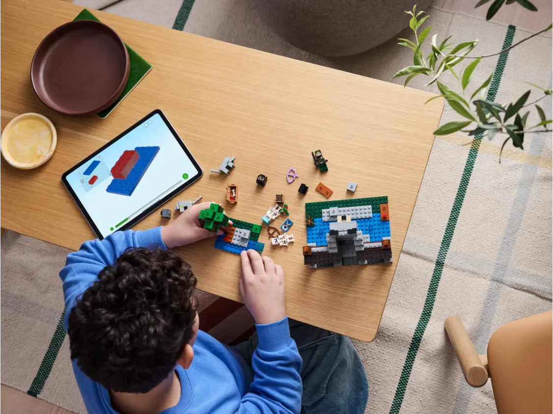 Child assembling the LEGO Minecraft The Wolf Stronghold Fortress Playset 21261 on a wooden table with an iPad nearby.