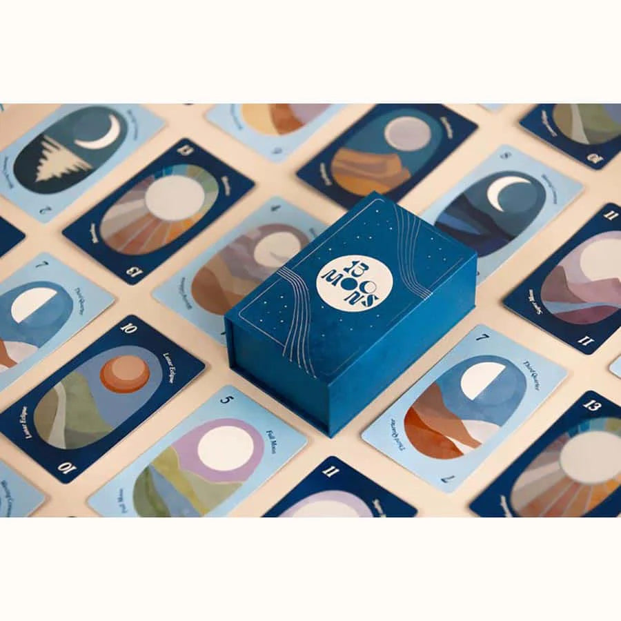 Blue box of "13 Moons: A Celestial Adventure!" surrounded by illustrated cards featuring moon phases and celestial designs.