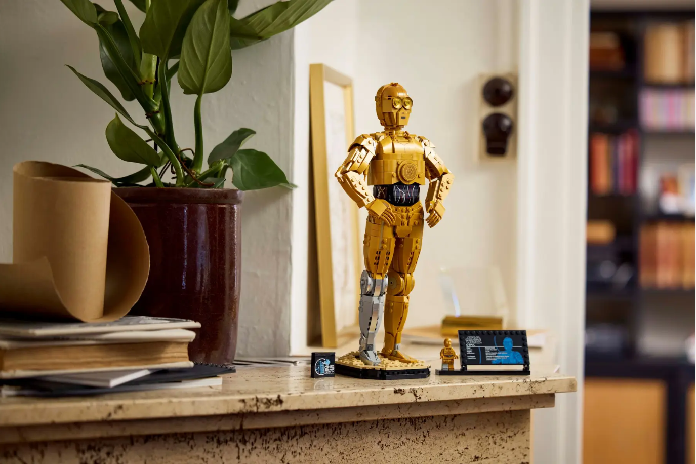 LEGO Star Wars C-3PO model stands on a shelf with a plant, books, and decorative items in the background.
