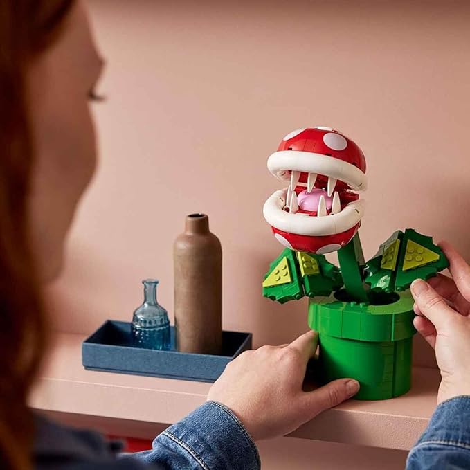 A person assembling the LEGO Piranha Plant (71426) model, featuring a vibrant green pot and a red-and-white flower.