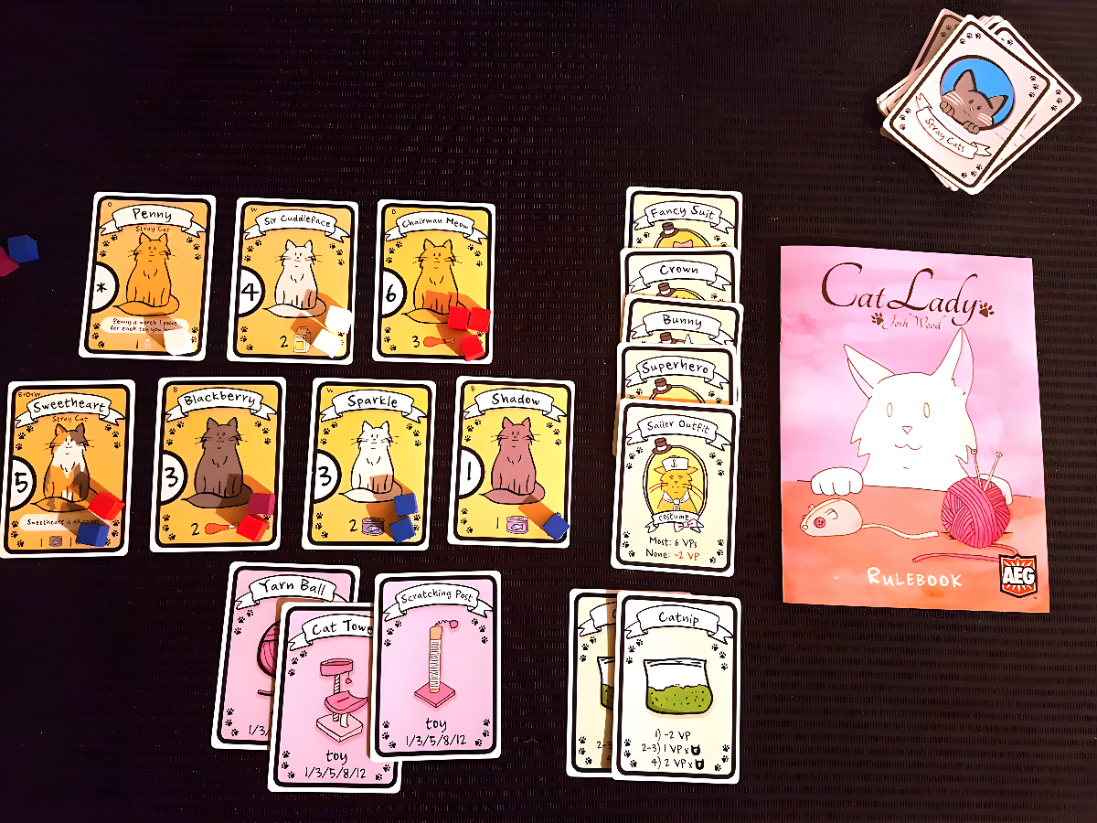 Colorful Cat Lady game components including cards featuring cats, a rulebook, and tokens on a black surface.