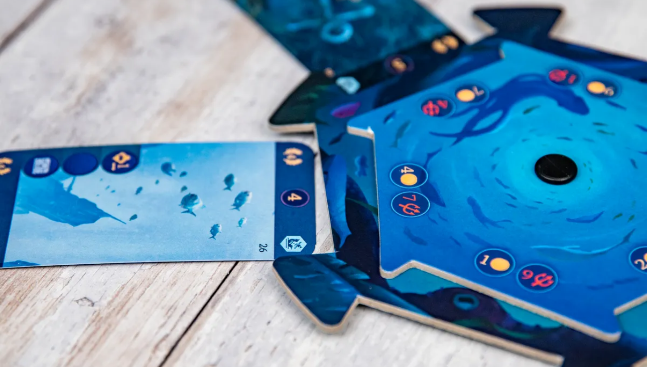 Aquatica Duellum game components featuring vibrant underwater-themed cards and hexagonal tiles on a wooden surface.