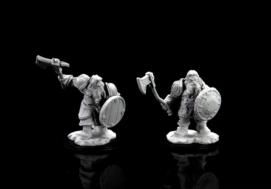 Unpainted miniatures of a male dwarf fighter, one wielding an axe and shield, the other with a hammer and shield.