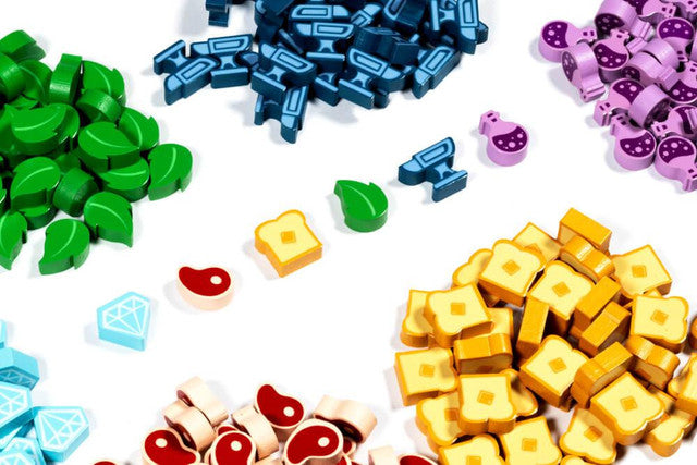 Colorful wooden resource tokens for the game Flamecraft, including leaves, potions, meat, and gems, arranged on a white background.