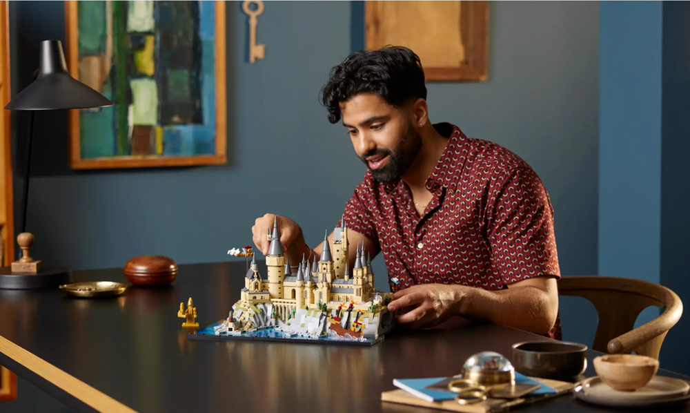 A person assembles the LEGO Harry Potter Hogwarts Castle and Grounds set on a table, showcasing detailed architecture and figures.