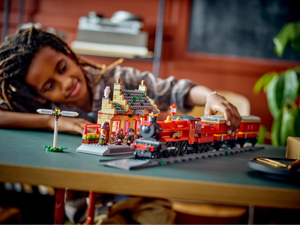 Child playing with LEGO Harry Potter Hogwarts Express and Hogsmeade Station set, featuring a train and detailed station.