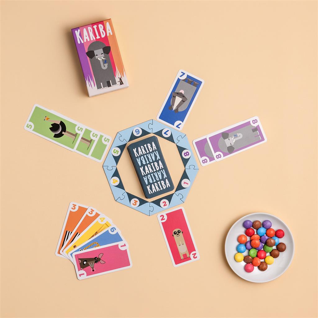 Colorful card game Kariba displayed with cards, game board, and a bowl of candies on a beige background.