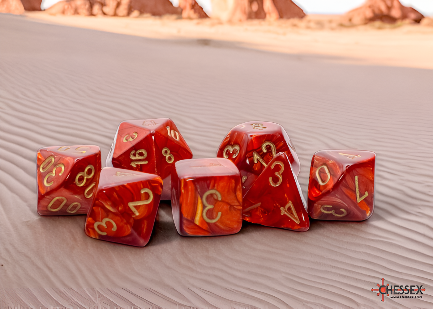 Scarlet and gold Chessex Scarab Mega-hedral dice set featuring seven polyhedral dice on a sandy surface.