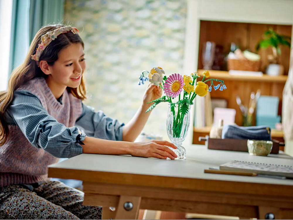 A girl assembles the LEGO Petite Sunny Bouquet set, featuring colorful flowers in a vase on a table.