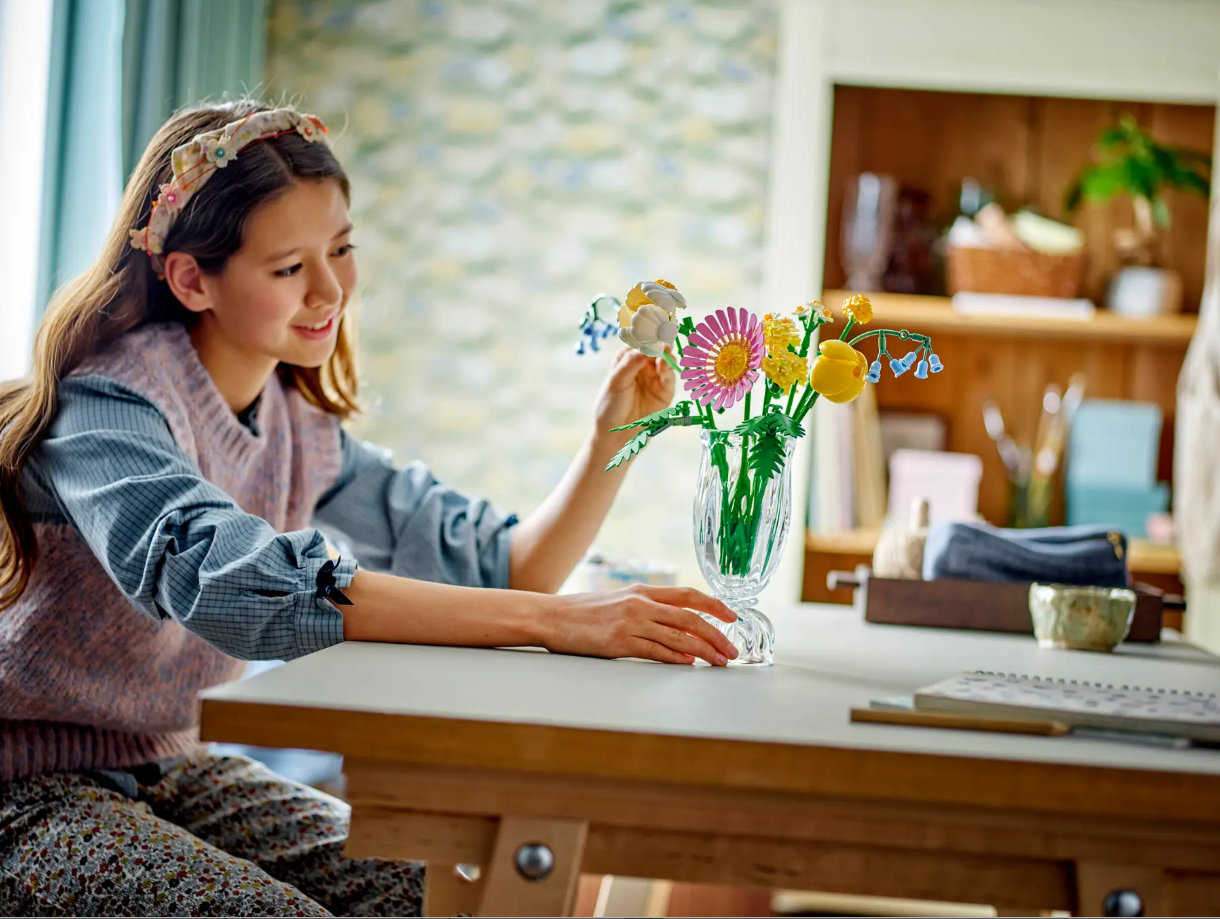 A girl assembles the LEGO Petite Sunny Bouquet set, featuring colorful flowers in a vase on a table.