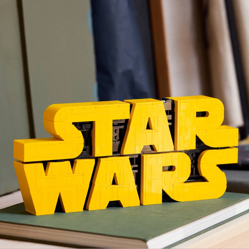 LEGO brick-built Star Wars logo displayed on a surface with fabric swatches in the background.