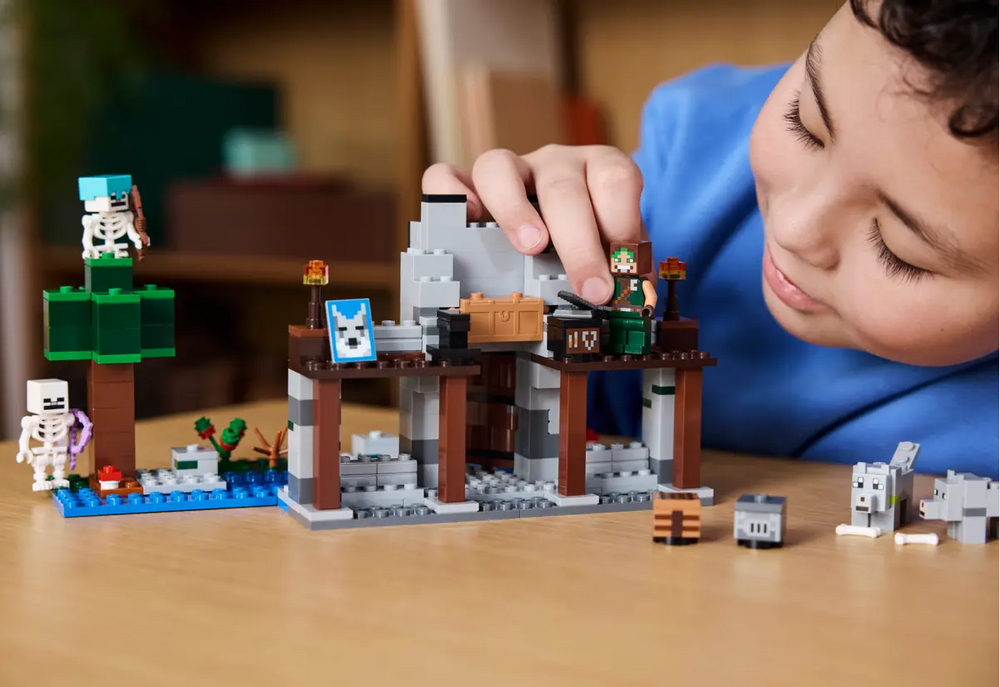 Child playing with LEGO Minecraft The Wolf Stronghold Fortress Playset 21261, featuring a fortress, skeletons, and accessories.