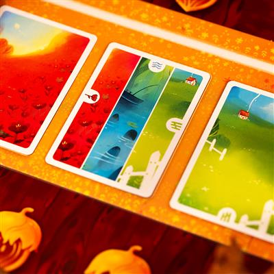 Colorful game cards from "Crossing the Woods" featuring vibrant landscapes of red, blue, and green with whimsical houses.