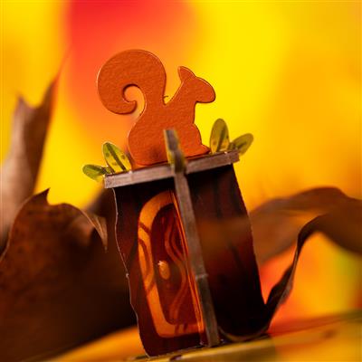 Colorful wooden squirrel figure atop a decorative game piece, surrounded by autumn leaves and a vibrant yellow background.